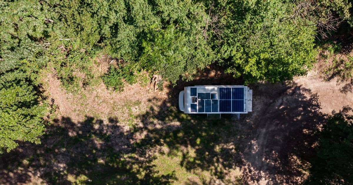 Pogled iz zraka na bivalni kombi s strešnimi solarnimi paneli, parkiran na gozdni jasi