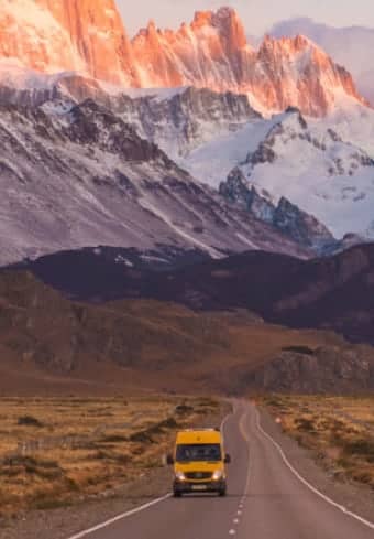 Rumen avtodom na odprti cesti pod zasneženim masivom Fitz Roy v Patagoniji